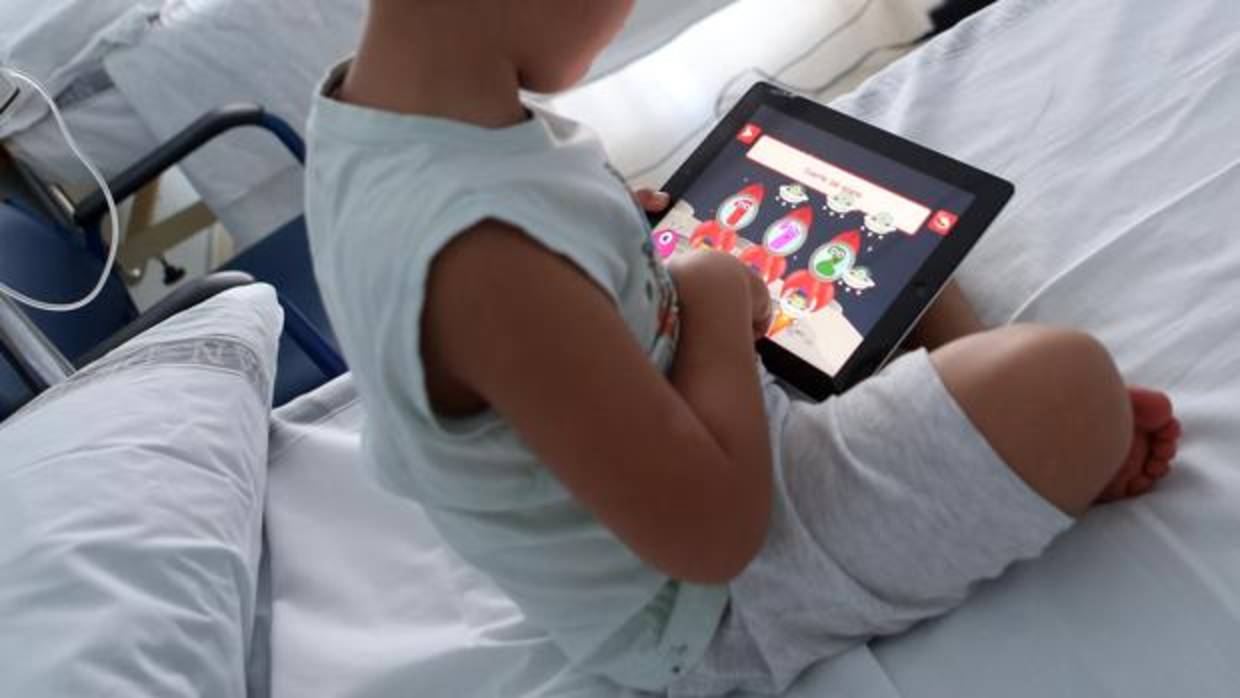 Un niño juega con la tablet en la cama del hospital