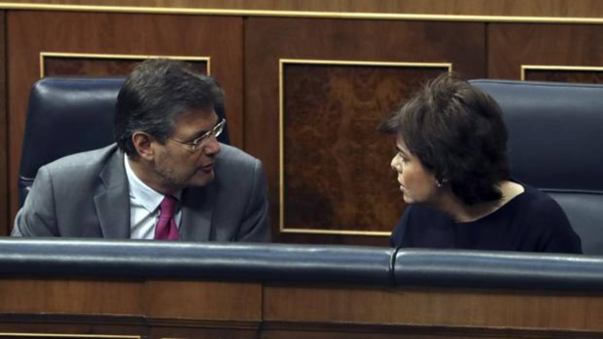 La vicepresidenta del Gobierno, Soraya Sáenz de Santamaría, conversa en su escaño con el ministro de Justicia, Rafael Catalá