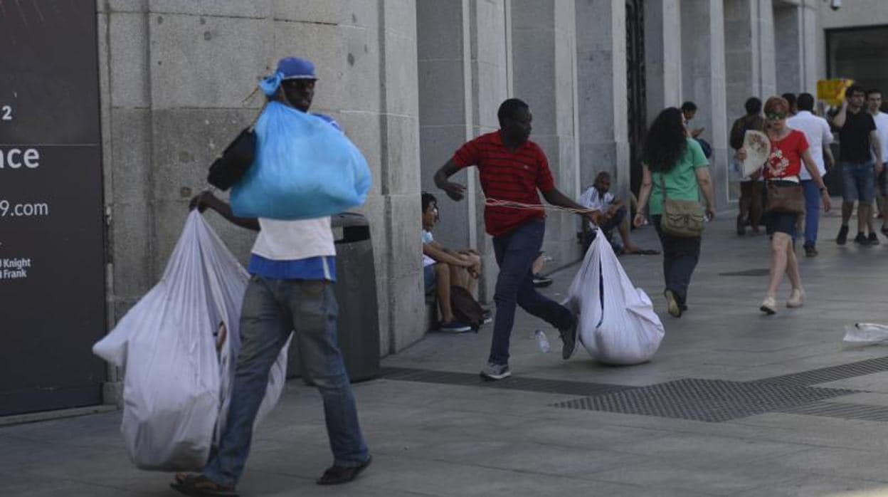 Unos manteros recogen sus productos en la Puerta del Sol al paso de la Policía Municipal
