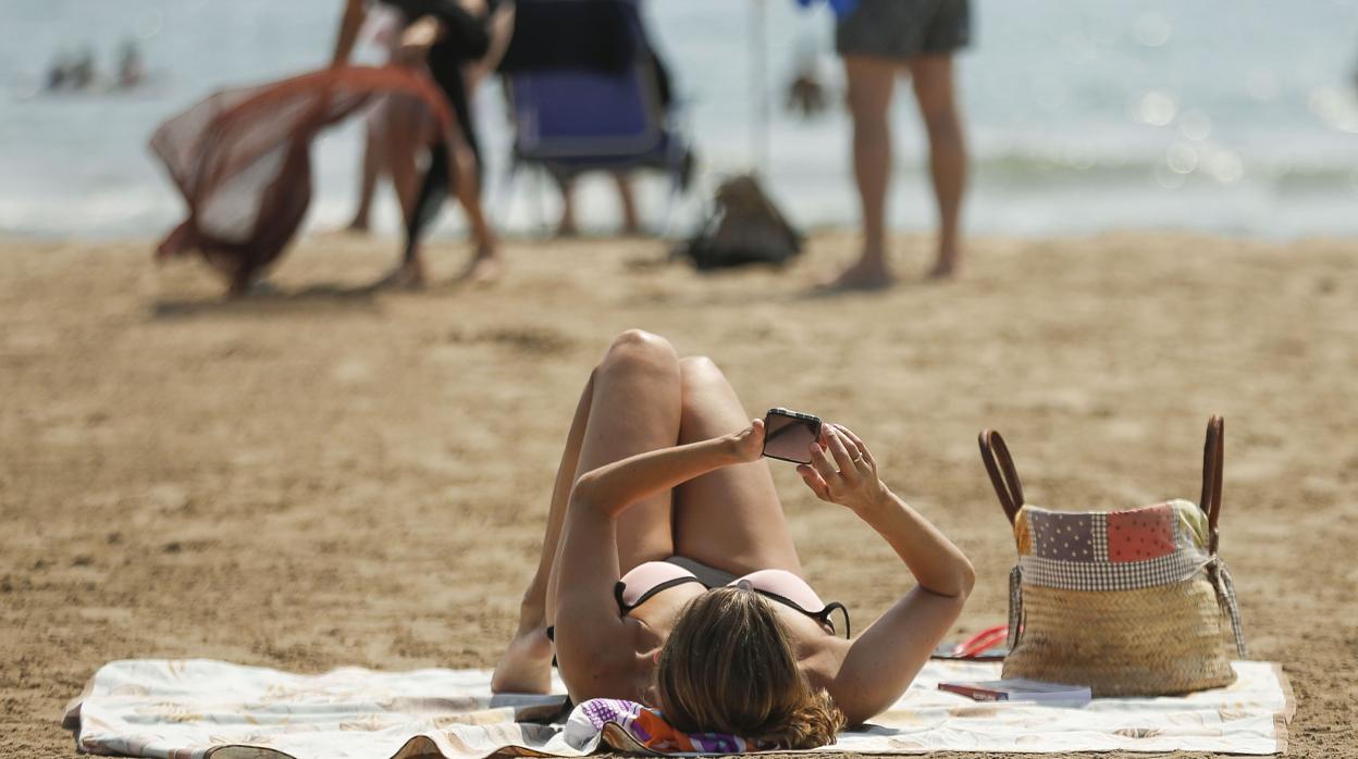 Una muier consulta su teléfono móvil en una playa alicantina