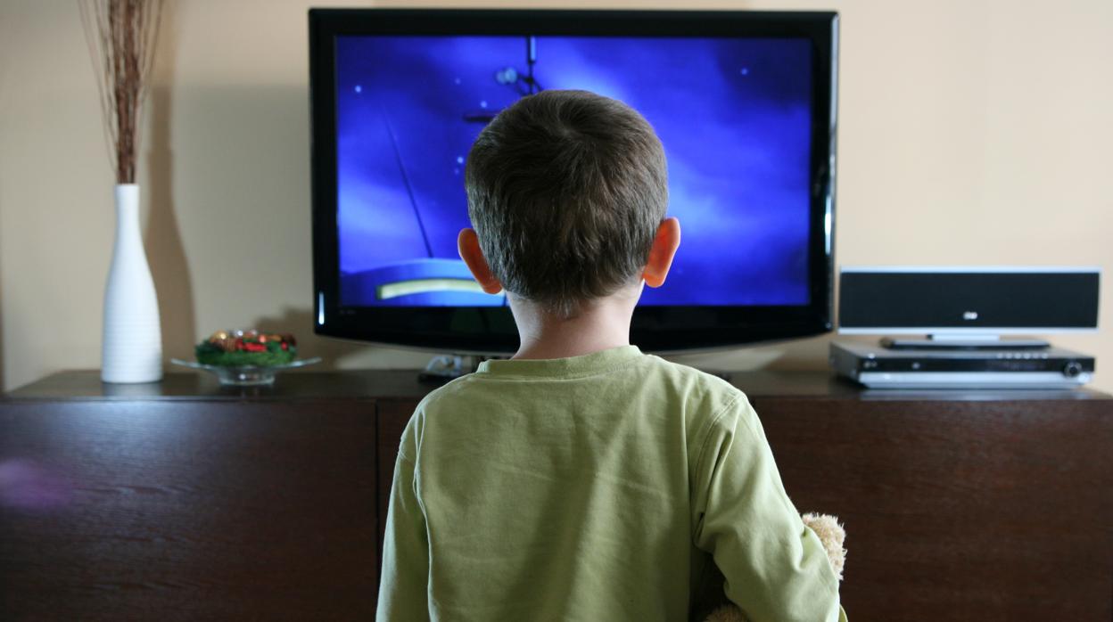 Un niño de 3 años viendo la televisión con un oso de peluche