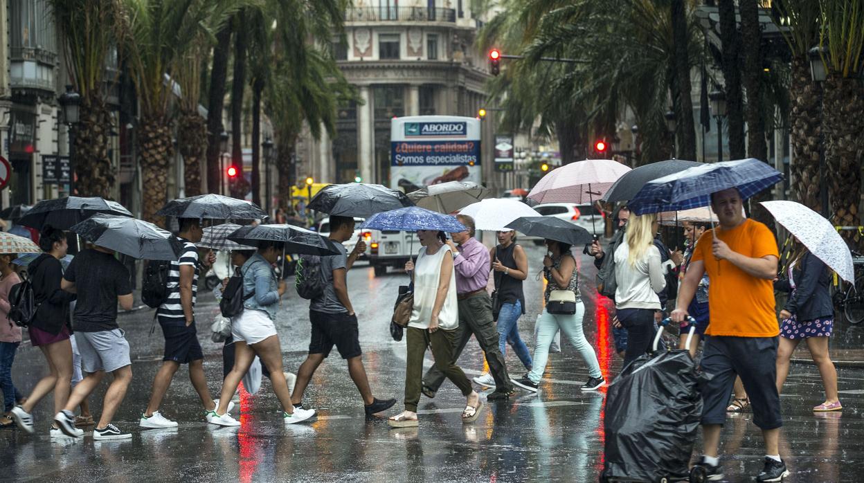 Imagen de peatones que se protegen con paraguas en la plaza del Ayuntamiento de Valencia.