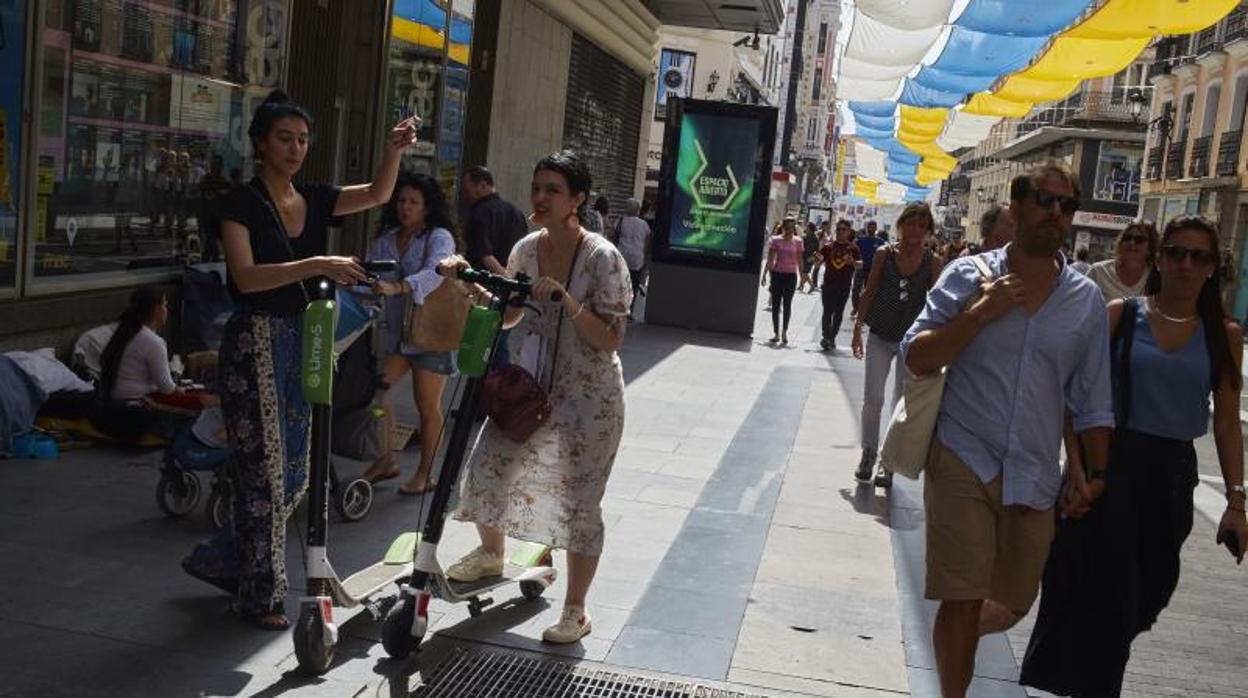 Dos mujeres se suben a dos patinetes eléctricos en la calle de Preciados