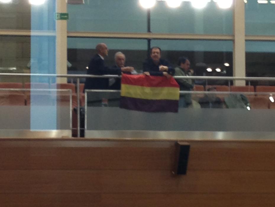 Momento en que un grupo de personas despliegan una bandera republicana en la tribuna pública del hemiciclo de la Asamblea de Madrid