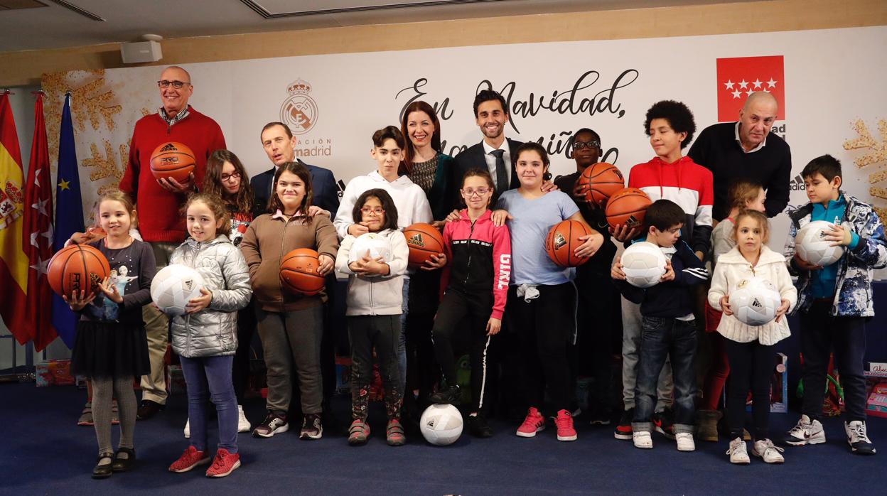 La consejera Lola Moreno (centro) con Butragueño y otros responsables del Real Madrid, y un grupo de niños que recibieron balones