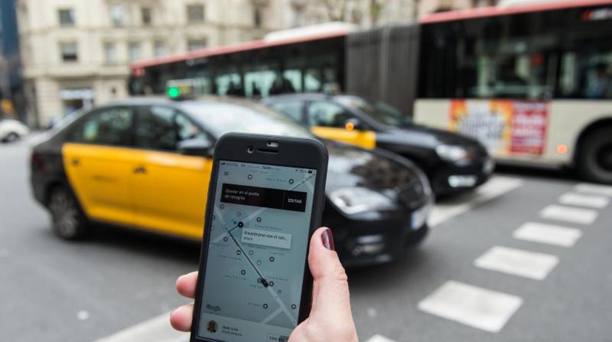 Un móvil con una aplicación de VTC abierta, en una call de Barcelona con taxis circulando