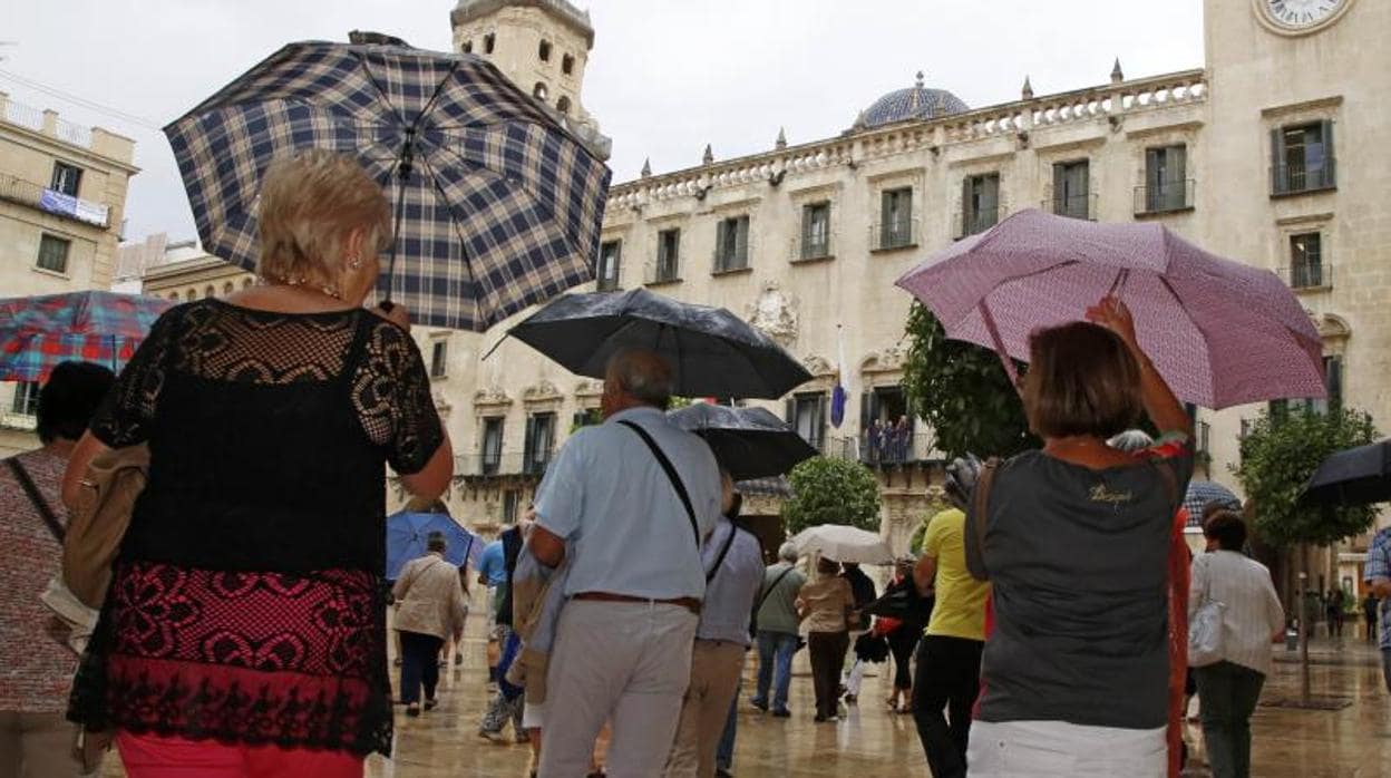 Espectadores de una procesión se protegen de la lluvia en la plaza del Ayuntamiento de Alicante