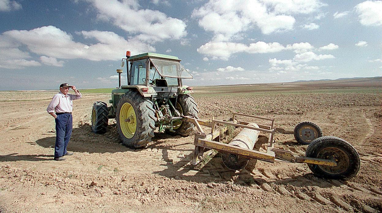 Un veterano agricultor mira al horizonte al pie de su tractor, en campos de Los Monegros