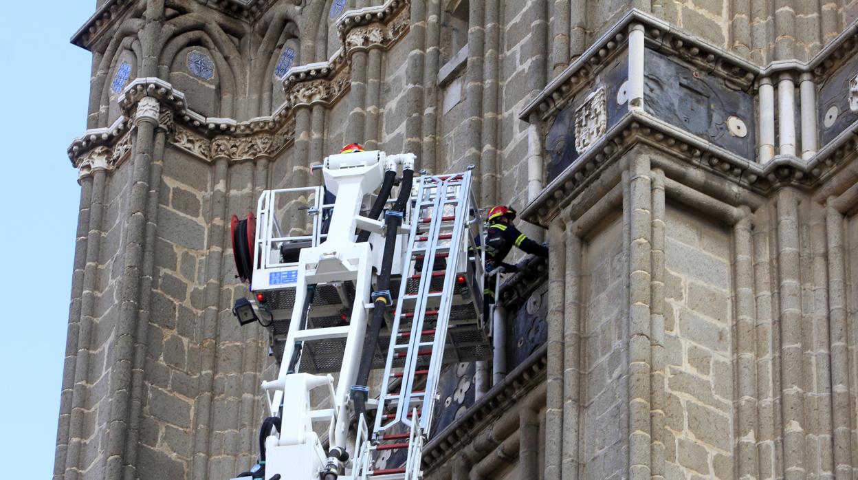 Bomberos, con una autoescala, revisan las cornisas de la torre de la catedral de Toledo