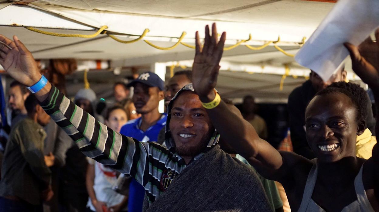 Los migrantes que quedaban a bordo del barco saludan momentos antes de desembarcar en la isla de Lampedusa