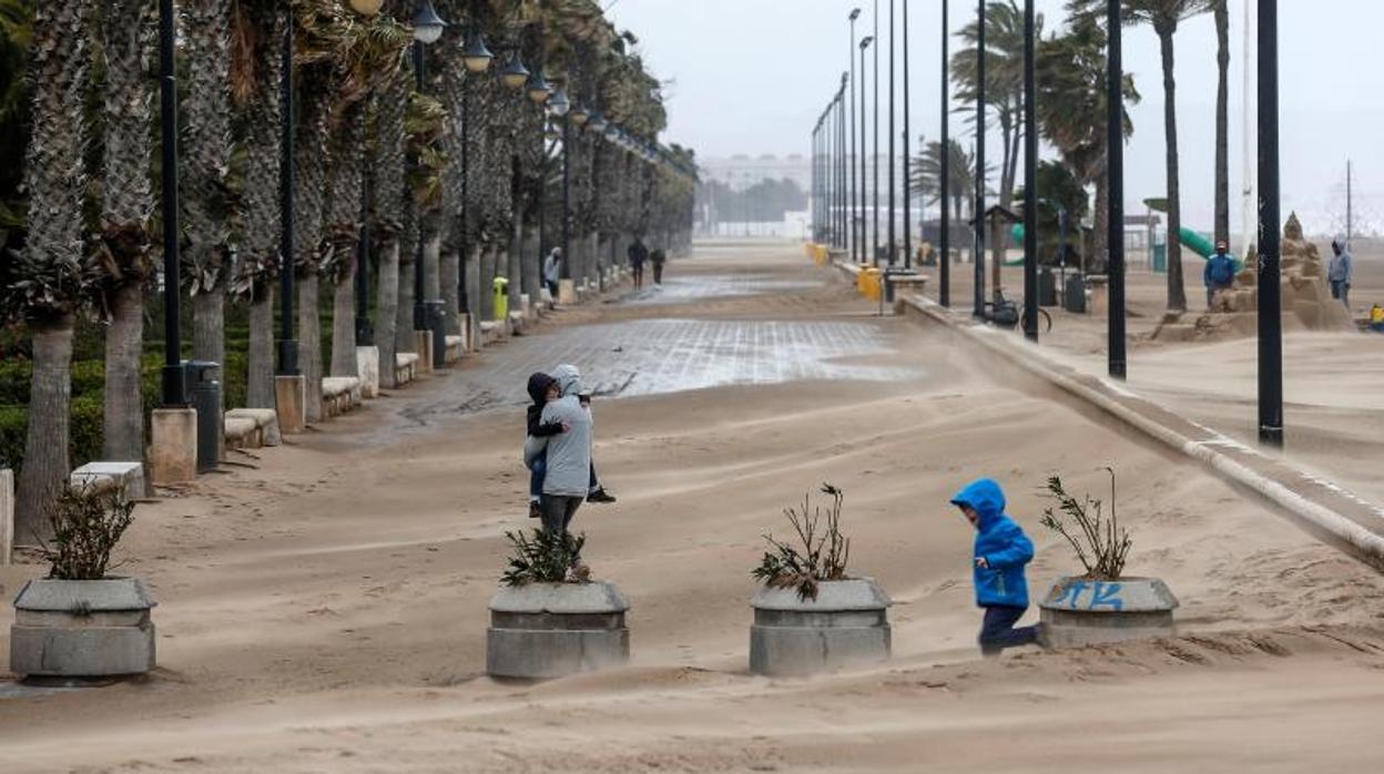 Varios transeúntes se protegen del viento en el paseo marítimo de Valencia en un temporal anterior