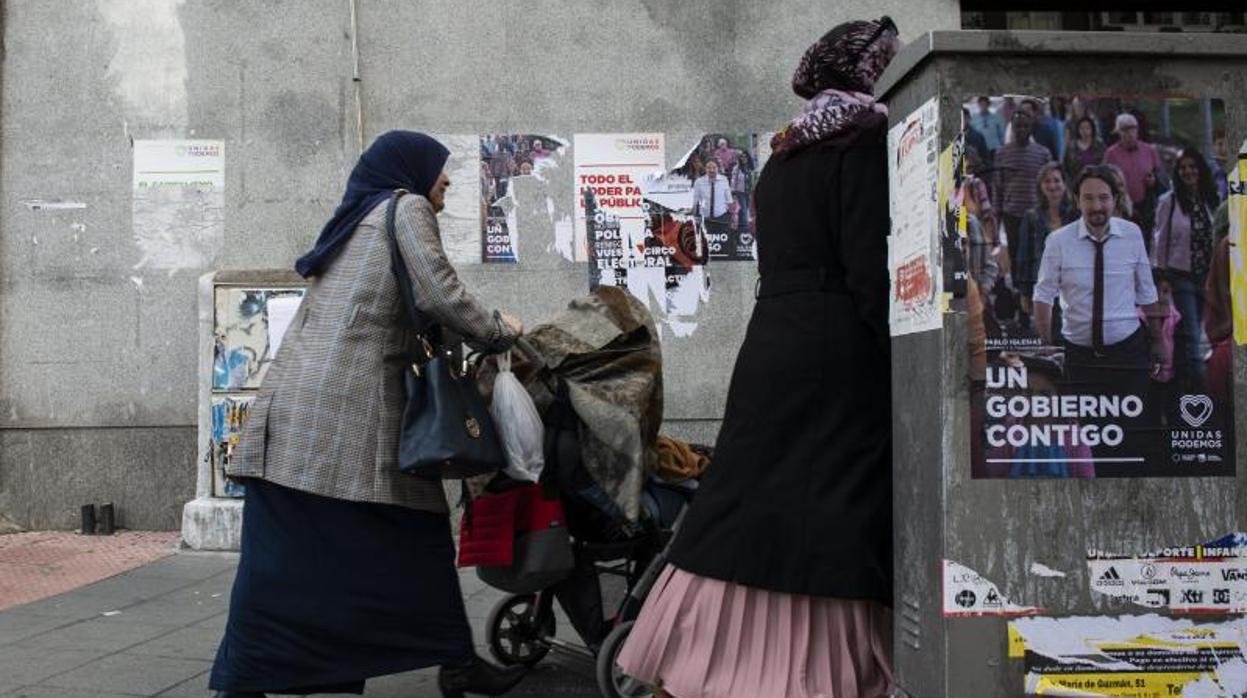 Dos mujeres pasean en Tetuán frente a la propaganda electoral de Podemos