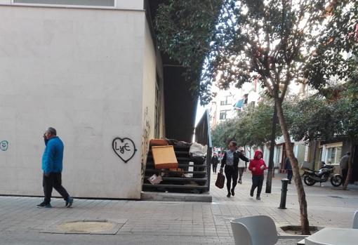 Transeúntes caminan junto al rincón ocupado por indigentes, frente a la terraza del bar