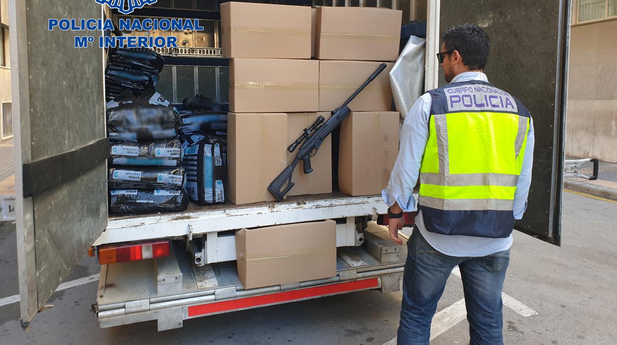 Un agente observa las cajas con plantas de marihuana y la carabina intervenidas a los dos traficantes