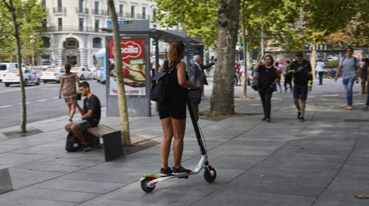 Imagen de una joven montada en un patinete eléctrico circulando por la acera