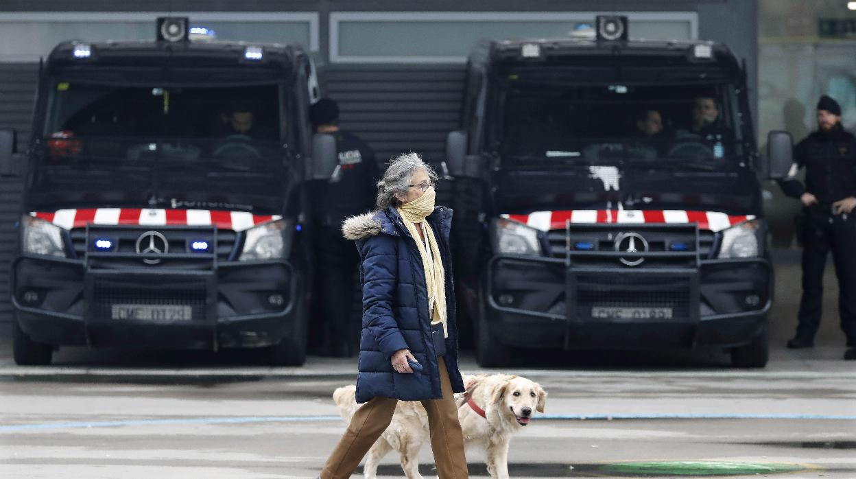 Una mujer pasea a su perro delante de unos furgones de los Mossos
