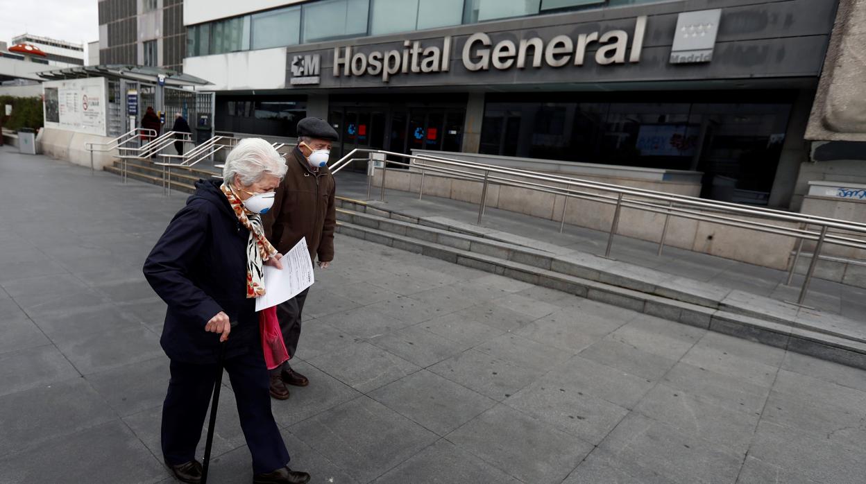 Dos ancianos caminan con mascarillas frente a un hospital de Madrid