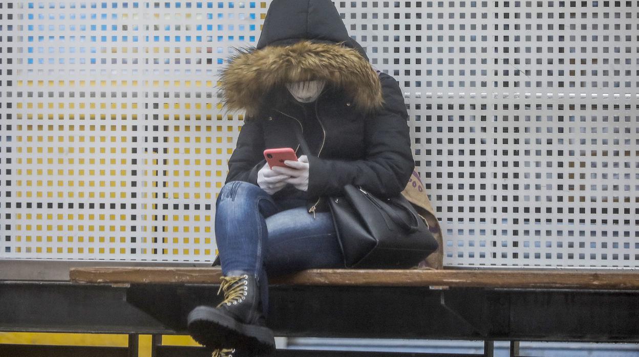 Imagen de una mujer consultando el móvil con guantes y mascarilla en Valencia