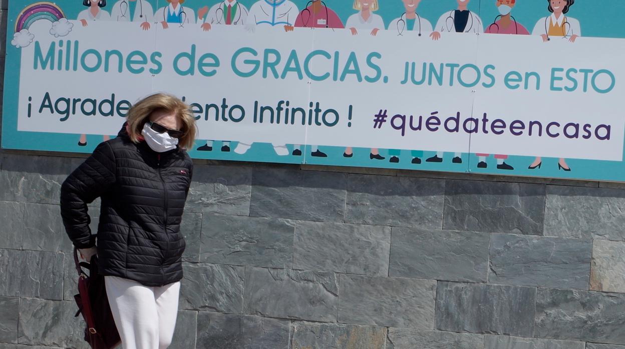 Una mujer con mascarilla pasa ante un cartel que pide quedarse en casa contra el coronavirus, en Zaragoza