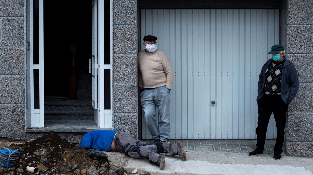 Dos vecinos de Beariz (Orense) observan cómo trabaja un operario en la reparación de una tubería, este miércoles