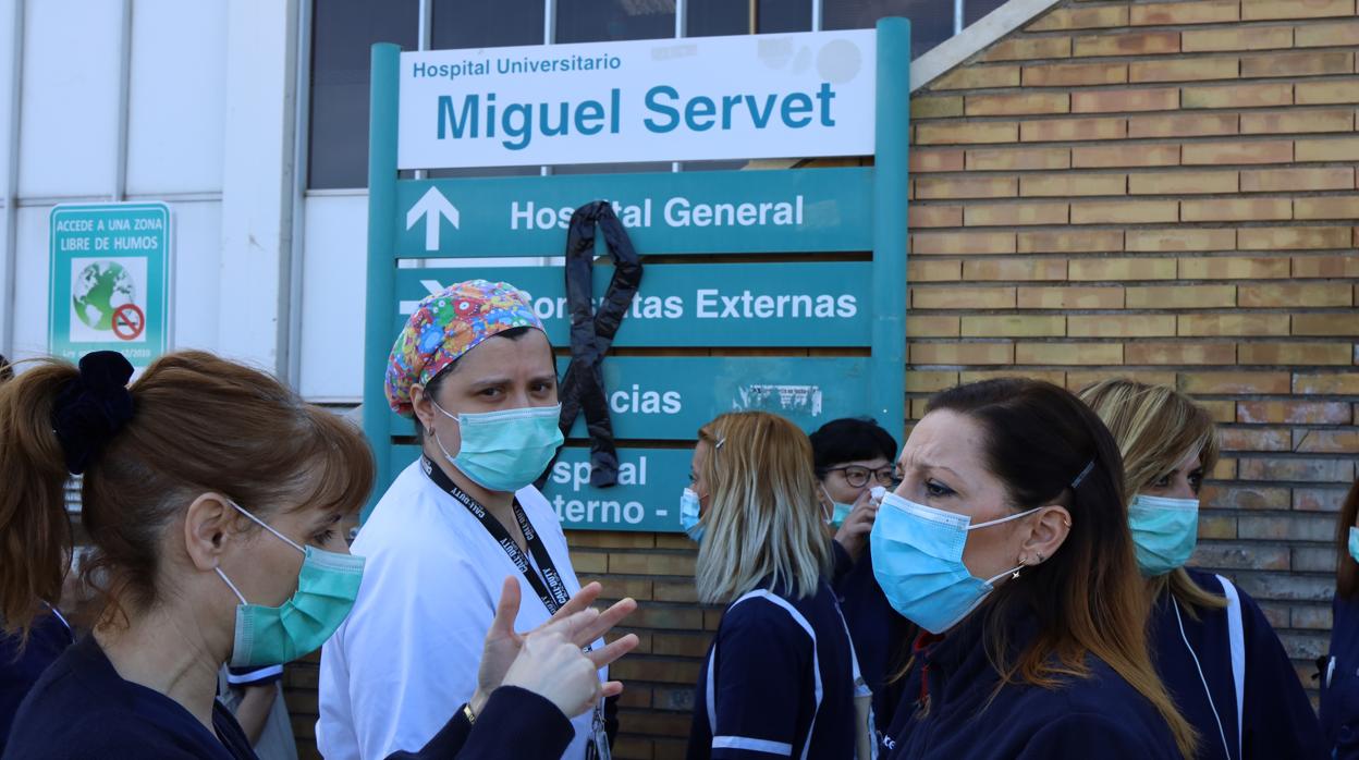 Personal sanitario ante un crespón negro colgado en el cartel del Hospital Miguel Servet de Zaragoza