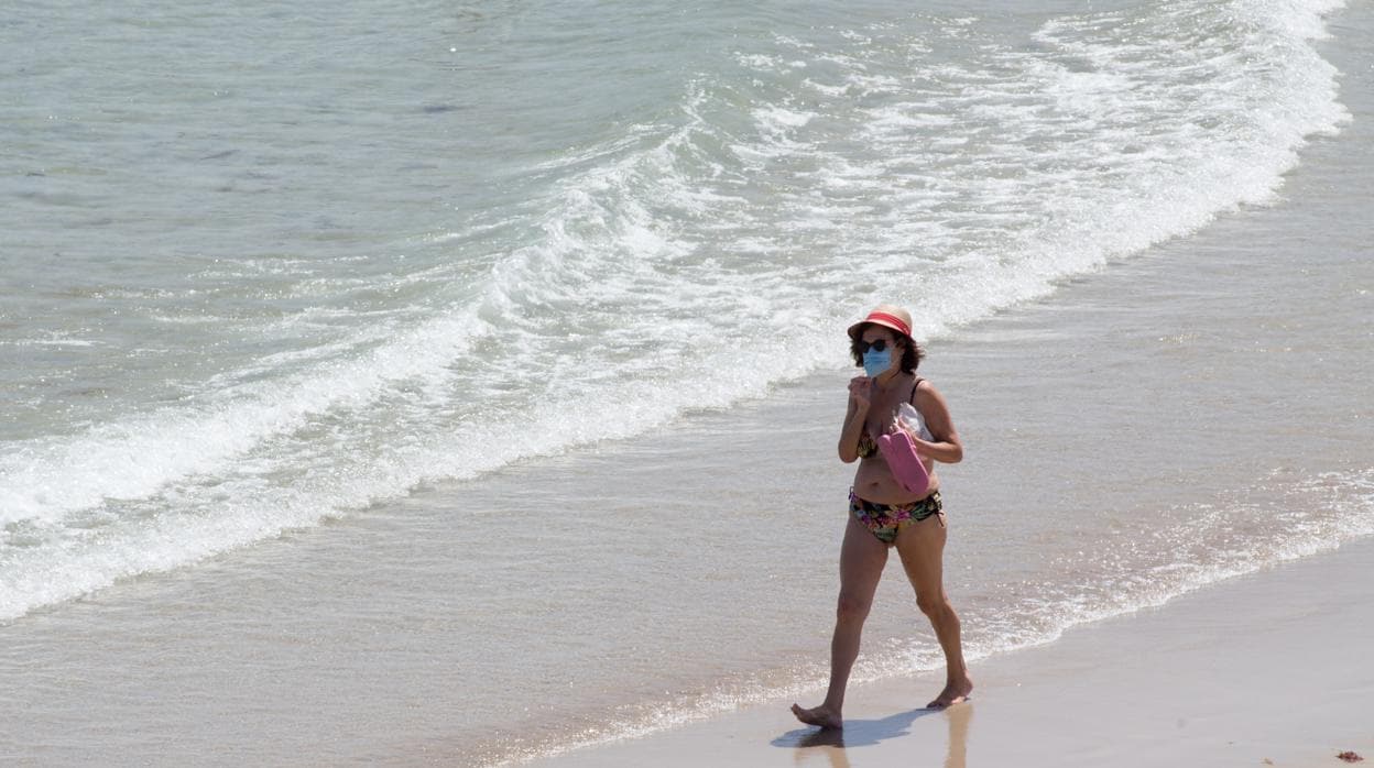 Una mujer protegida con mascarilla pasea por la Playa de A Rapadoira en Foz, en la comarca de A Mariña
