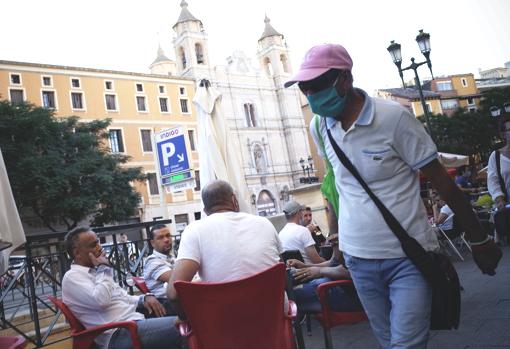 Un peatón pasa, con la mascarilla obligatoria, ante mesas llenas de consumidores sin mascarilla