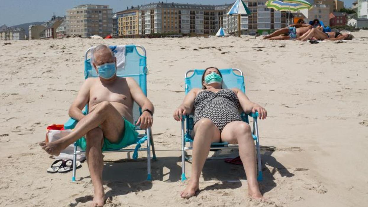 Dos personas toman el sol en una playa de Foz, en A Mariña lucense