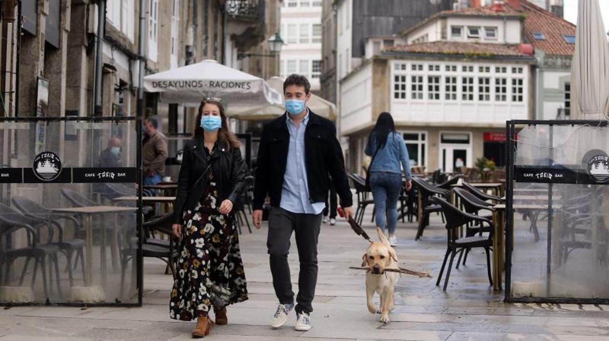 Dos personas pasean a su perro por el centro de Santiago, provistos de mascarillas