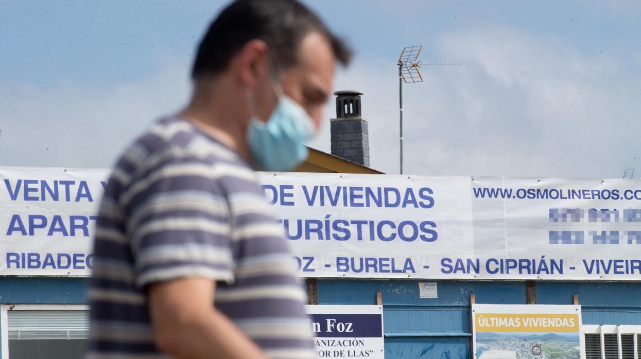 Un hombre camina junto a un cartel de viviendas en venta en A Mariña (Lugo)