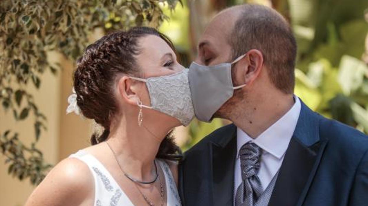 Una pareja de novios se dan el beso nupcial con mascarilla durante la pandemia