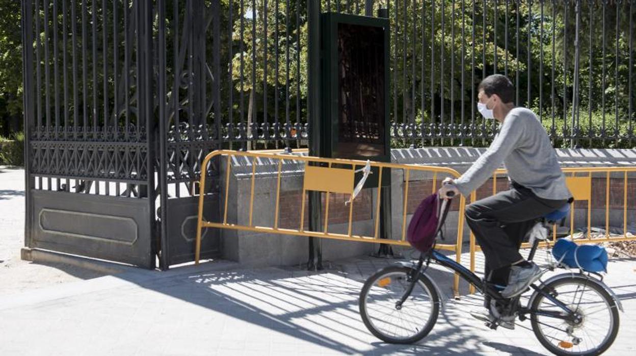 Un ciclista accede al Retiro por una de las puertas en las que ya han instalado una de las pantallas informativas para evacuar el parque