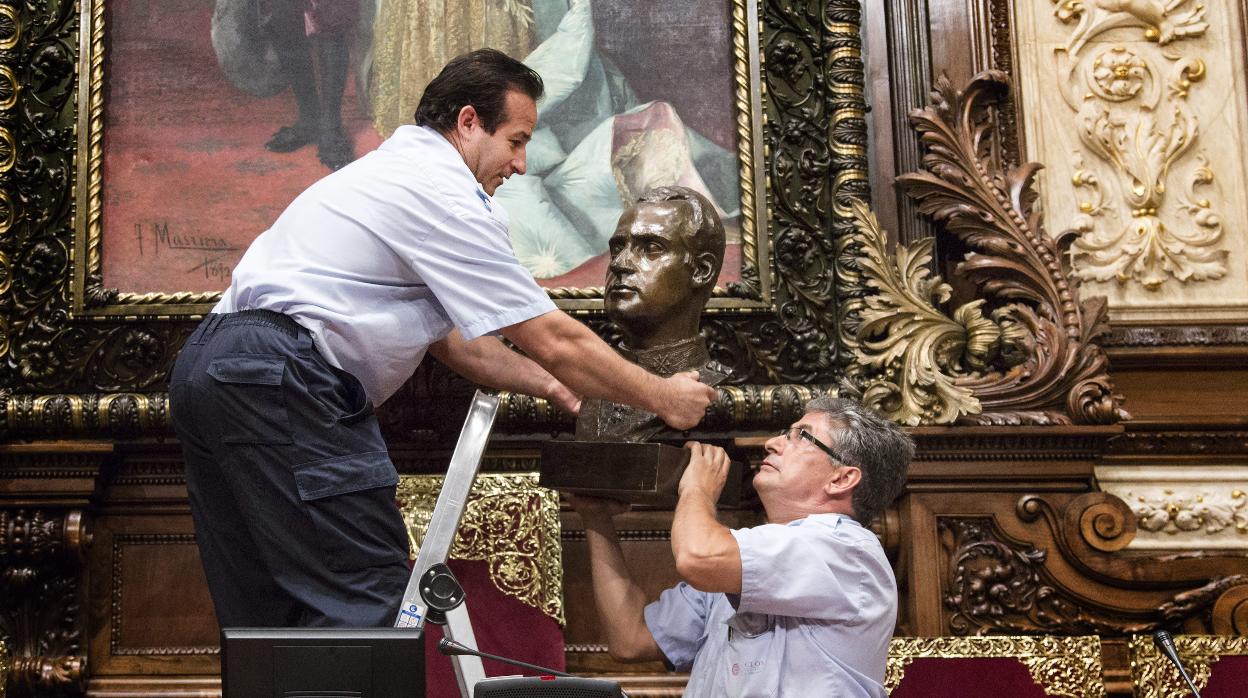 Dos operarios municipales retiran el busto del Rey Juan Carlos I que hay en el Salón de la Reina Regente, donde se celebran los plenos municipales del Ayuntamiento de Barcelona