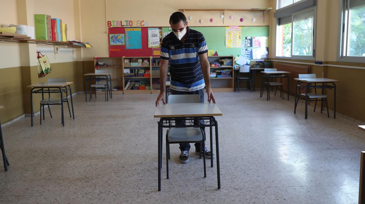 n profesor con mascarilla prepara un aula, durante la vuelta parcial a las clases de junio