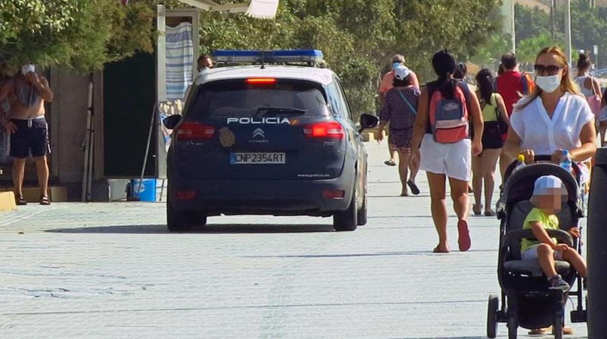 Un coche patrulla de la Policía Nacional y paseantes junto a la playa del Postiguet