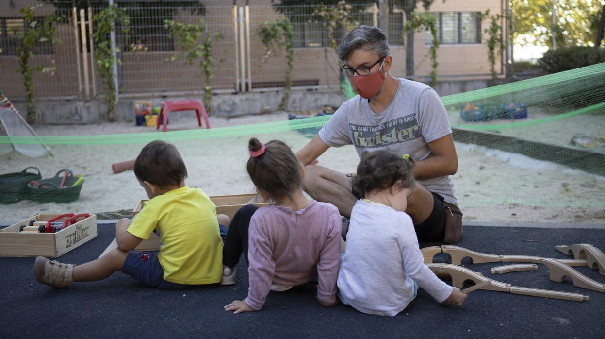 Tres pequeños se divierten en el patio de Las Nubes bajo la atenta mirada de un educador