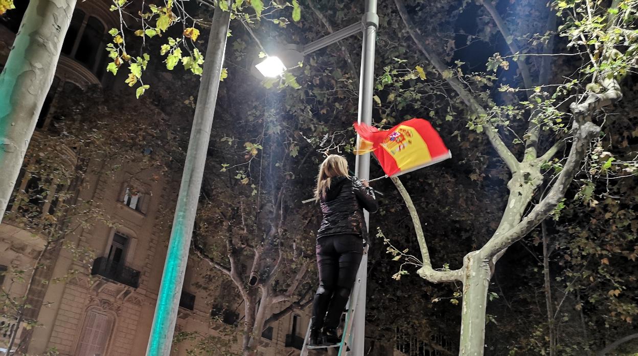Una mujer instala una bandera de España en una farola del centro de Barcelona, la pasada noche