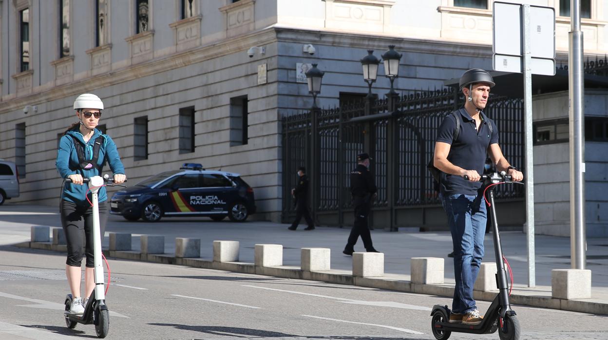 Dos usuarios de patinete, circulando por una calle de Madrid