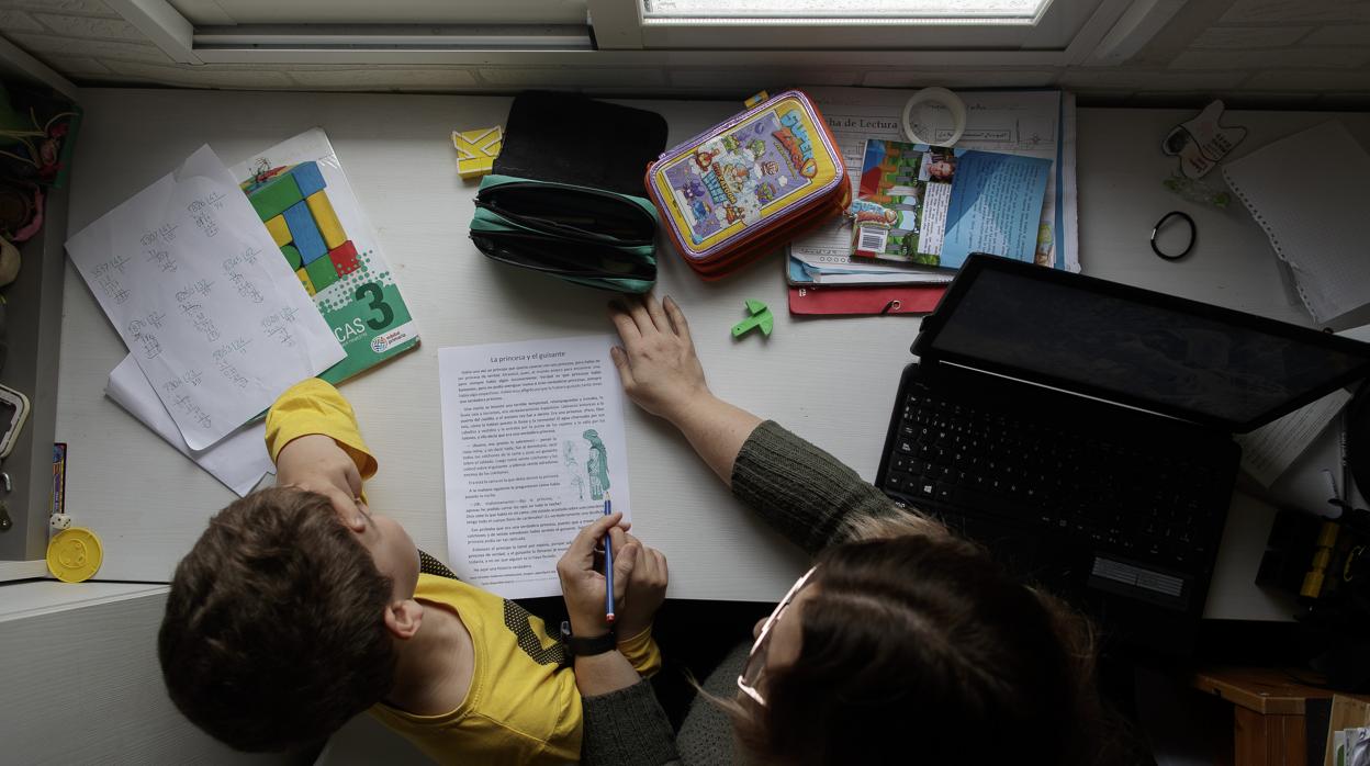 Un niño realizando las tareas escolares en casa, ayudado por su madre