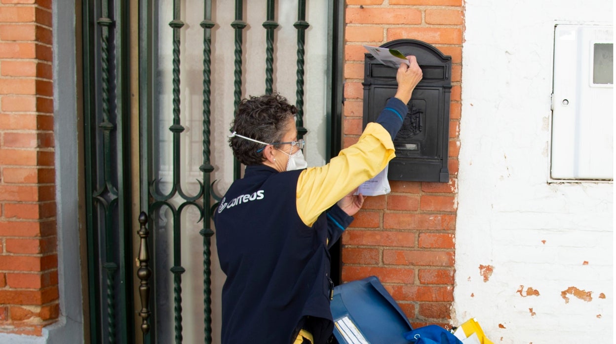 Una trabajadora de Correos, con mascarilla, introduce una carta en un buzón