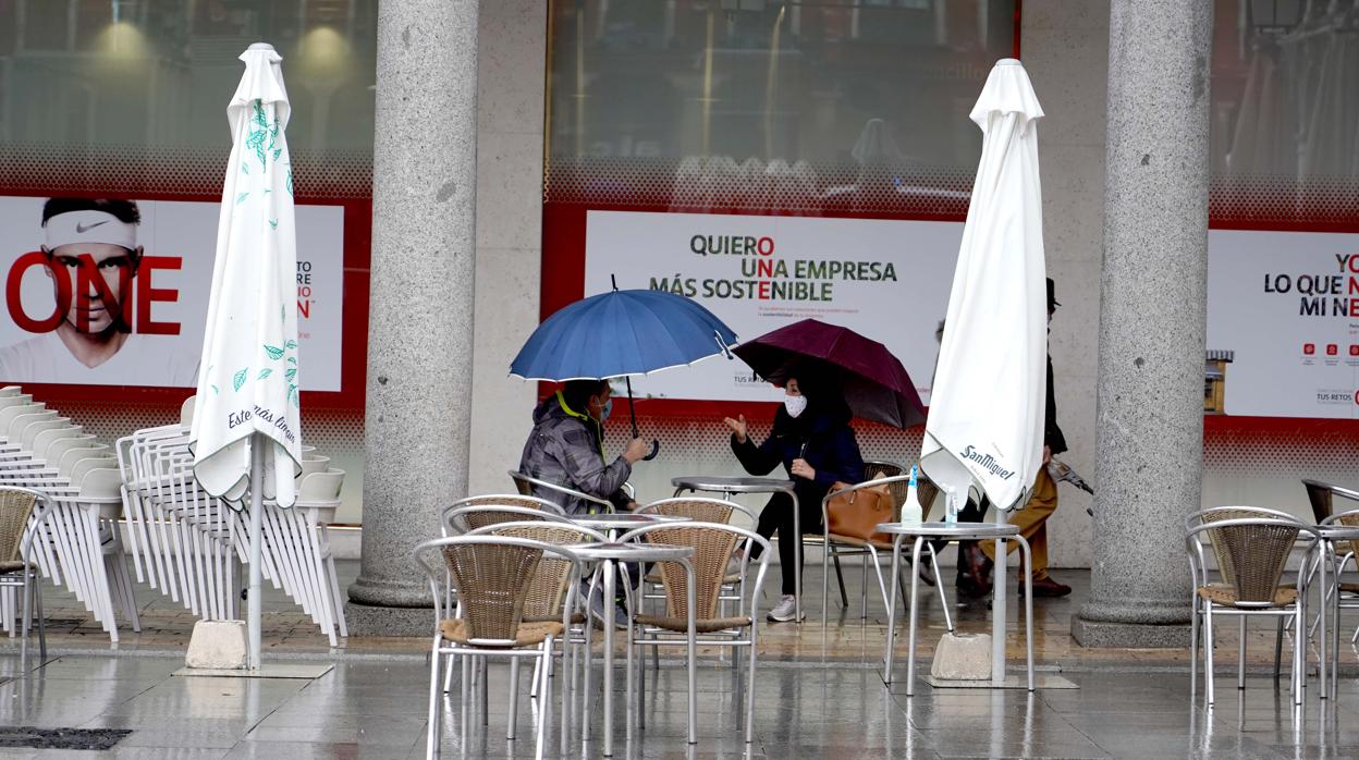 Una pareja se protege de la lluvia en una terraza de la Plaza Mayor de Valladolid