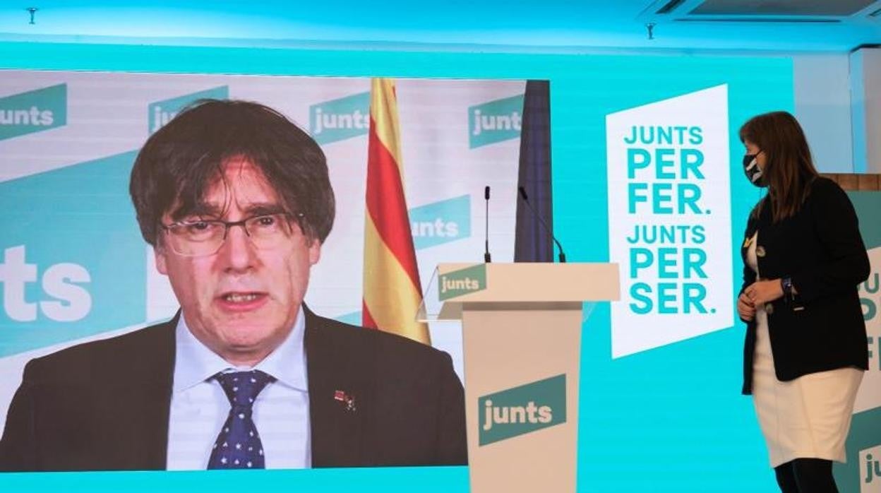 La número 2 de JxCat por Barcelona, Laura Borrás, observa al número 1 del partido por Barcelona, Carles Puigdemont (pantalla), durante una rueda de prensa para valorar los resultados obtenidos el 14-F