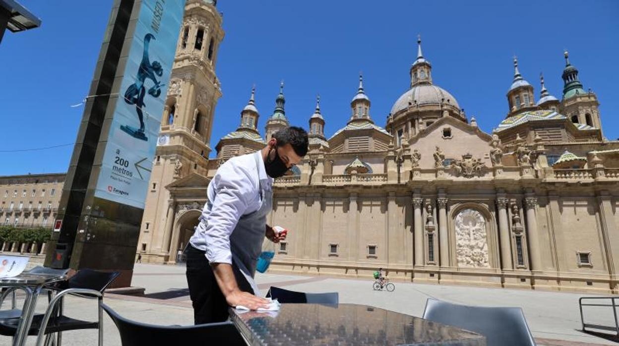 Un camarero prepara la mesa de una terraza frente a la Basílica del Pilar, en Zaragoza