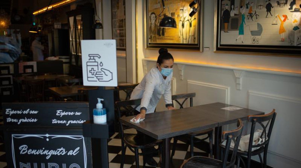 Una trabajadora limpia una mesa en el interior de un local de Barcelona