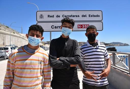 Tres menores posan frente a un cartel de la carretera nacional N-352, que comunica Ceuta con la frontera de El Tarajal