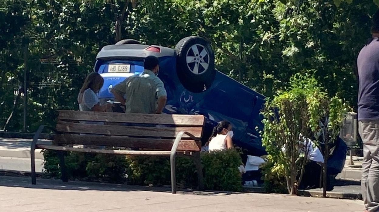 El coche volcado en la calle y el conductor, atendido por transeúntes