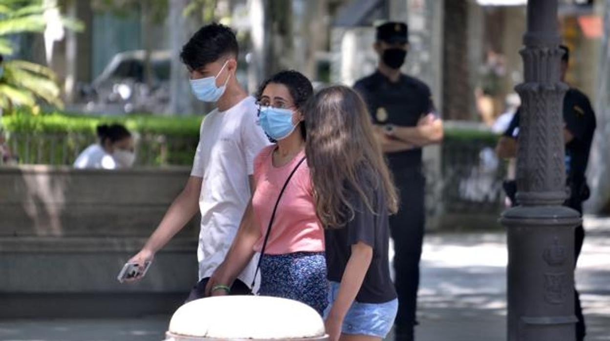 Tres jóvenes pasean por una calle con sus mascarillas puestas ante la mirad de dos policías nacionales