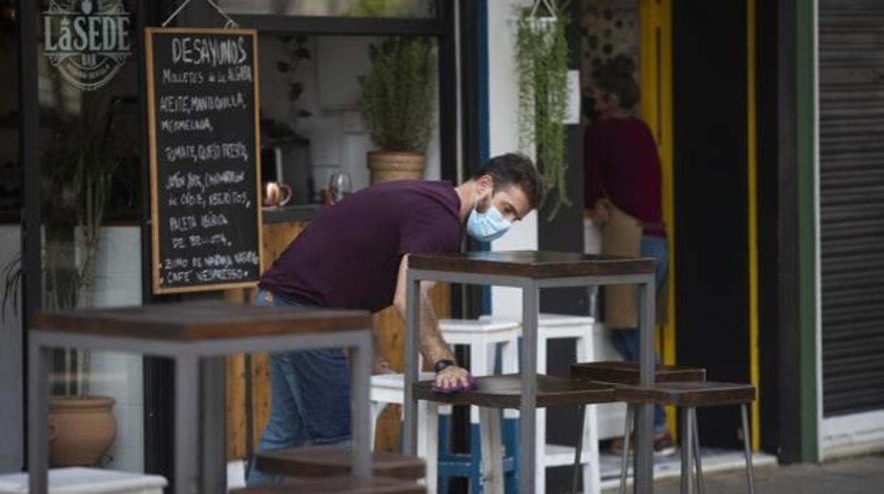 Un camarero limpia las sillas y las mesas de un bar