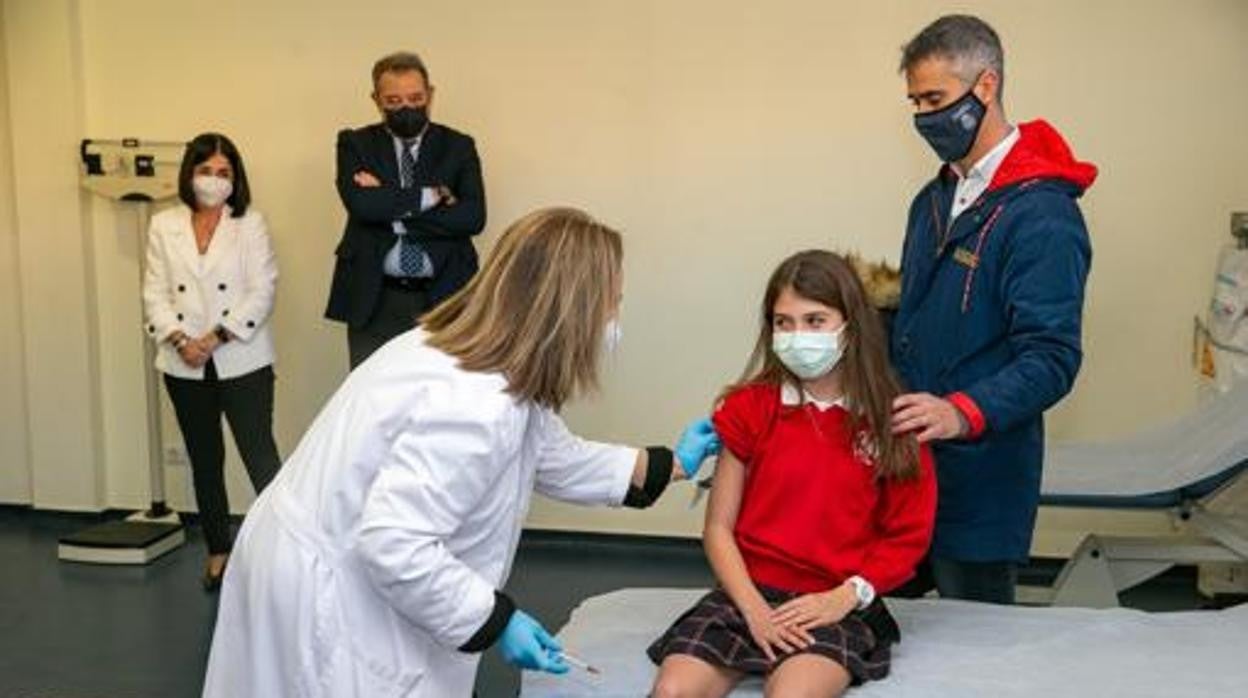 Una sanitaria vacuna a una niña ante la atenta mirada de la ministra de Sanidad y el consejero regional