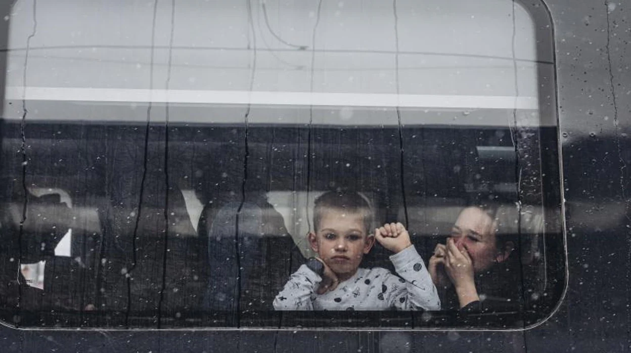 Una mujer trata de contener las lágrimas tras su hijo, que se despide a través del cristal del tren